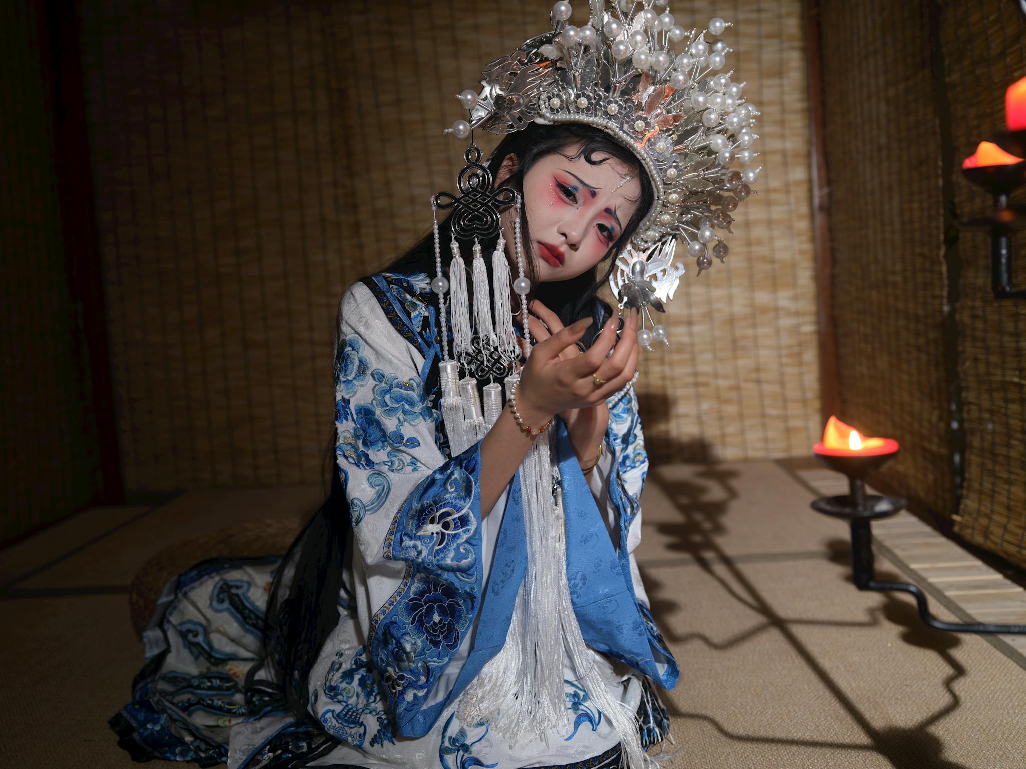 A female performer in traditional Chinese opera attire poses indoors with dramatic makeup and an ornate headdress.