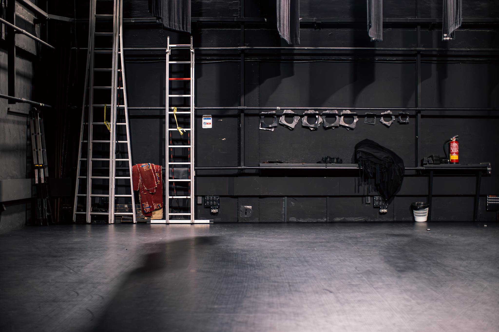 A quiet theater stage with ladders and equipment, ready for setup.